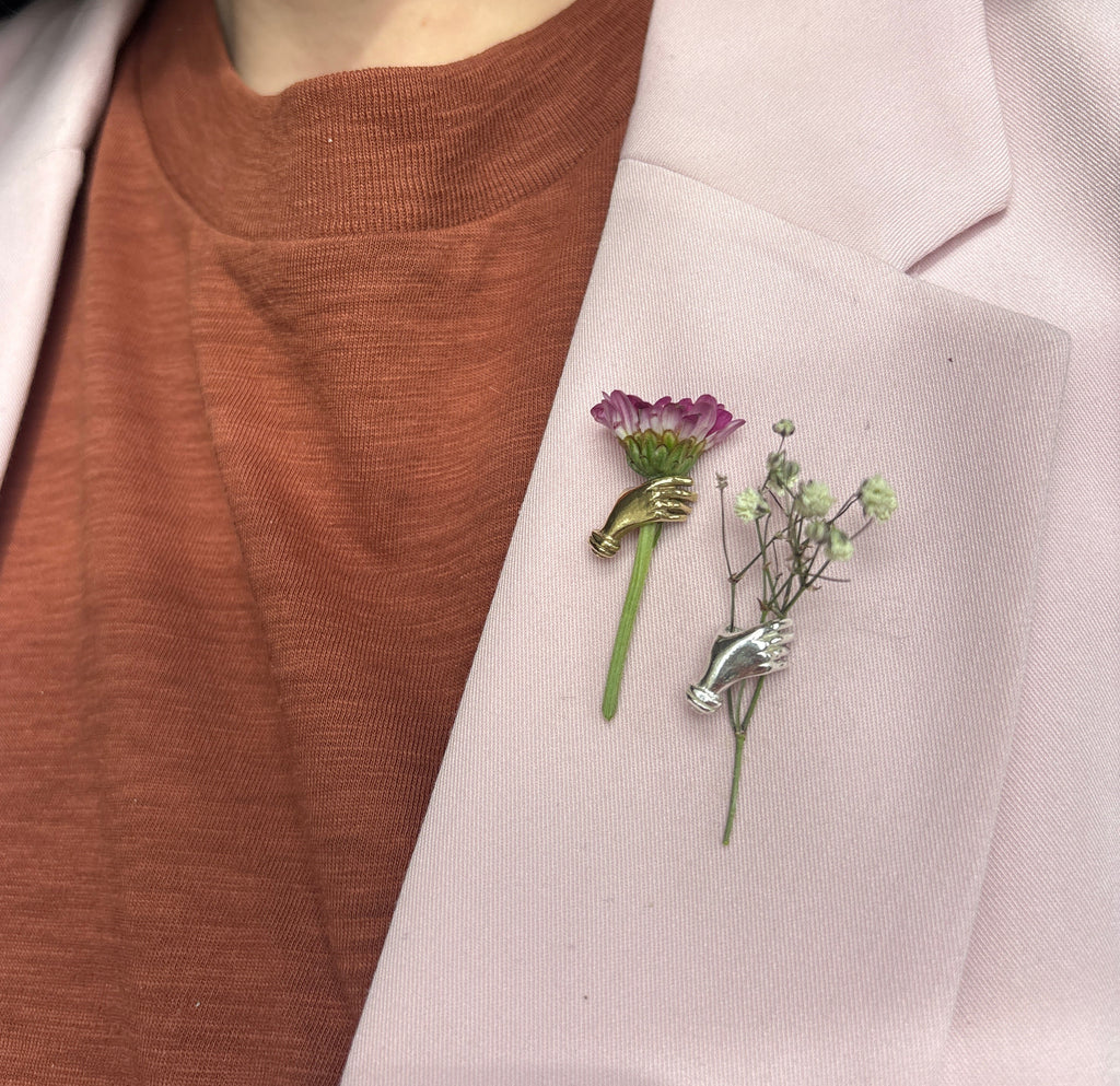 a whimsical hand lapel pin that has the capability to hold a small bunch of lightweight flowers 