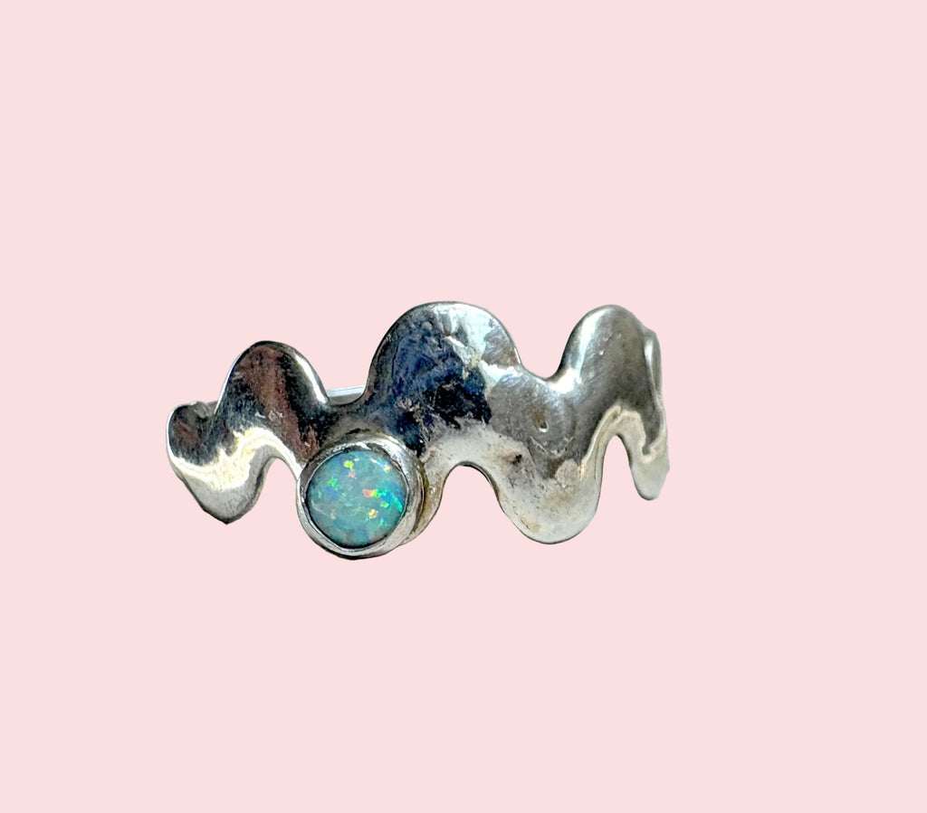 Silver ring with a central opal stone on a white surface